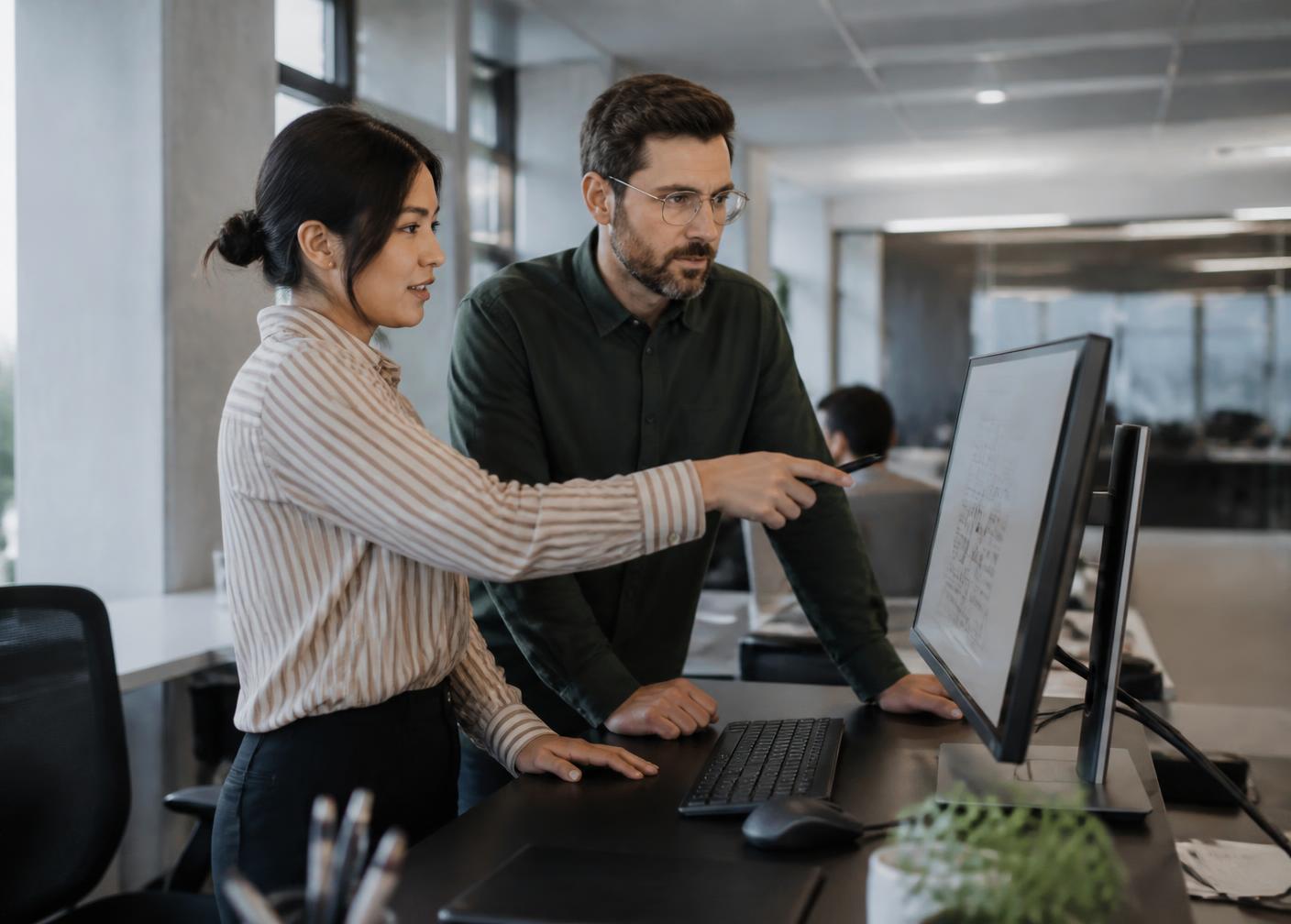 Two colleagues reviewing a shared document together on a monitor in an open office